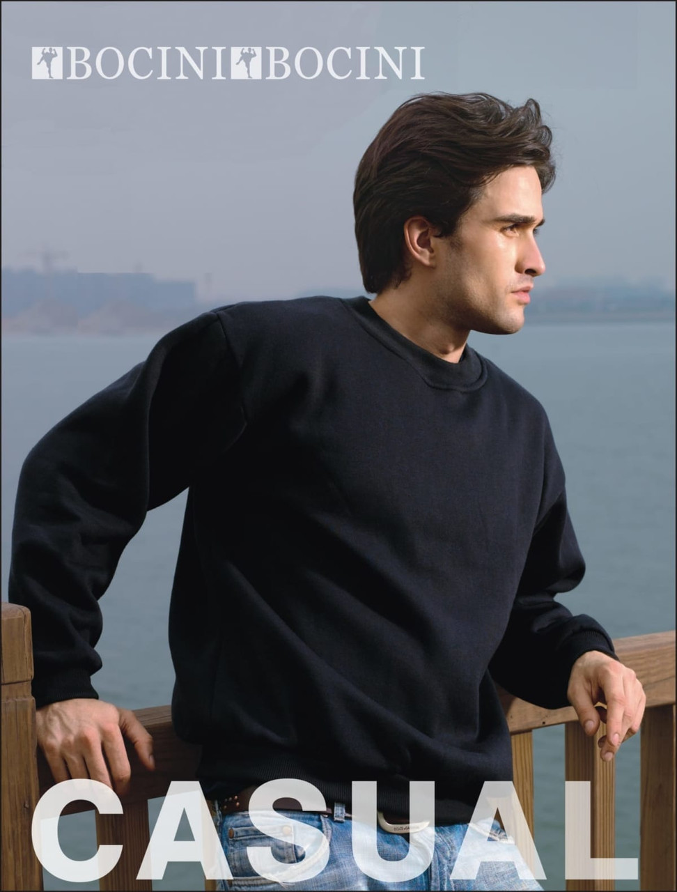 A black unisex crew neck fleece sweater worn by a man, positioned by a wooden railing near water. The image includes a logo.
