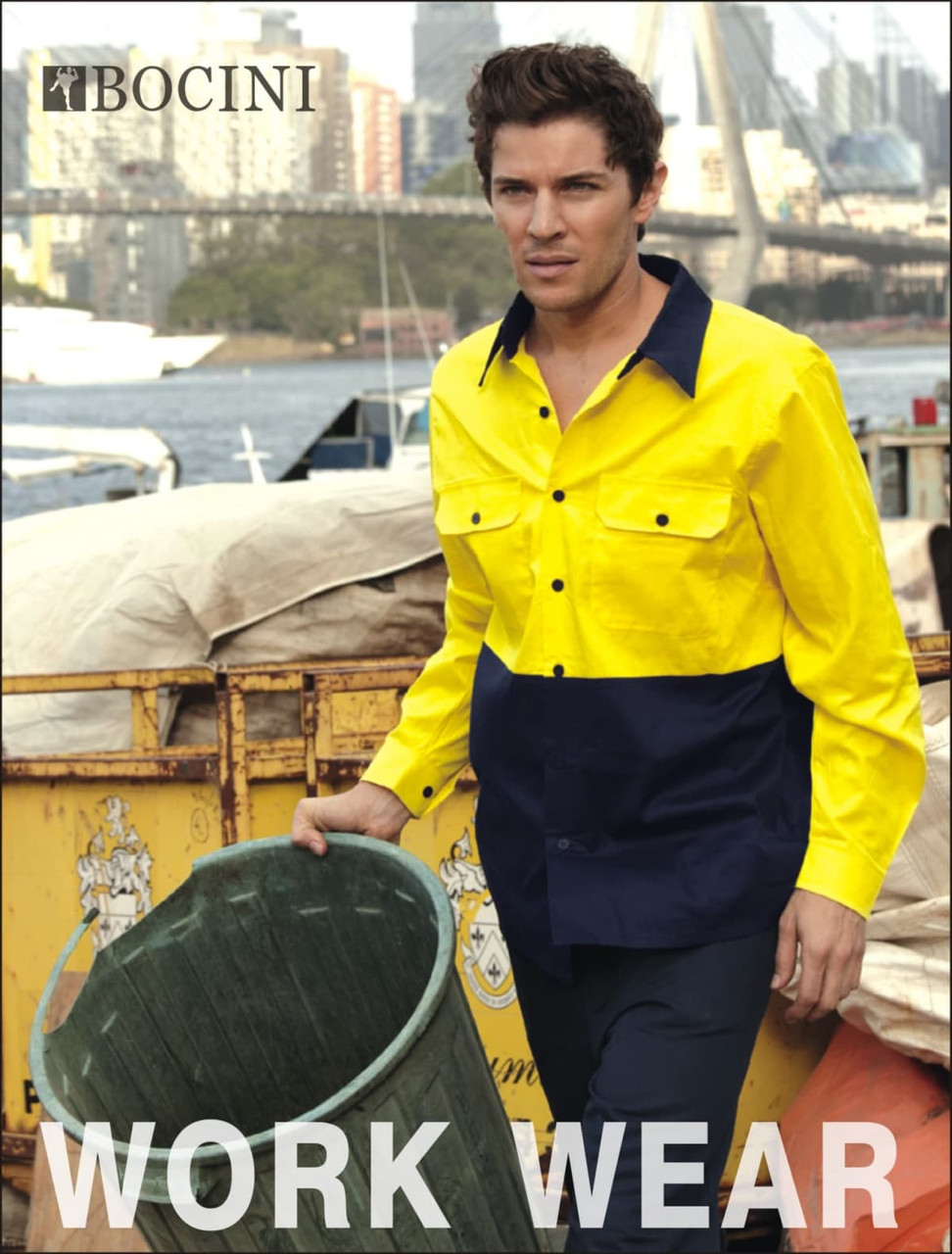 A man wearing a bright yellow and navy blue hi-vis cotton twill shirt, standing near a bin by the water.