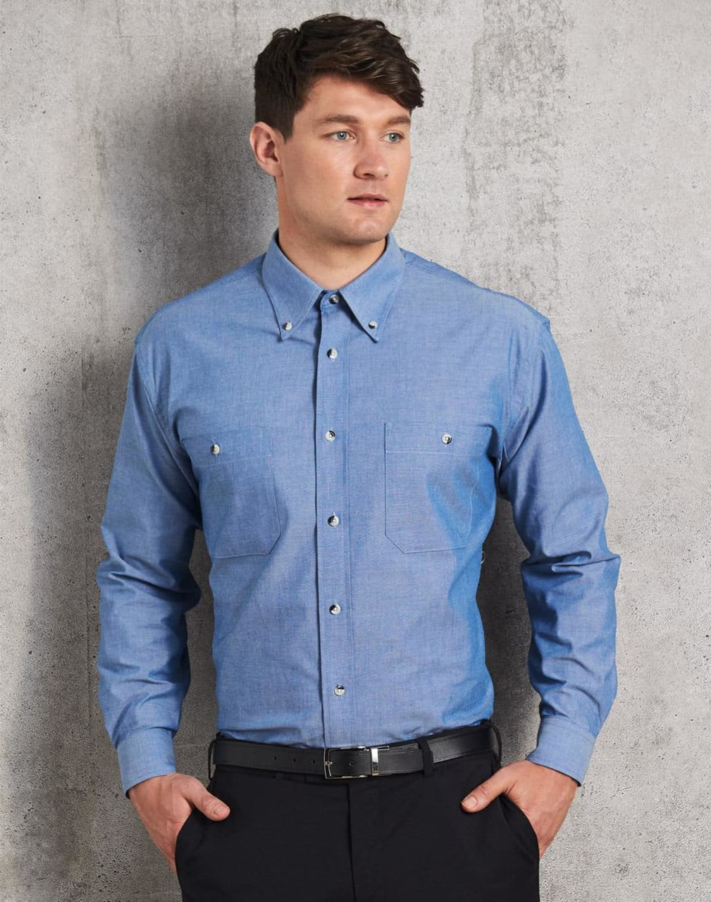 A blue chambray long sleeve shirt with two chest pockets and a button-up front, featuring a subtle brand logo.