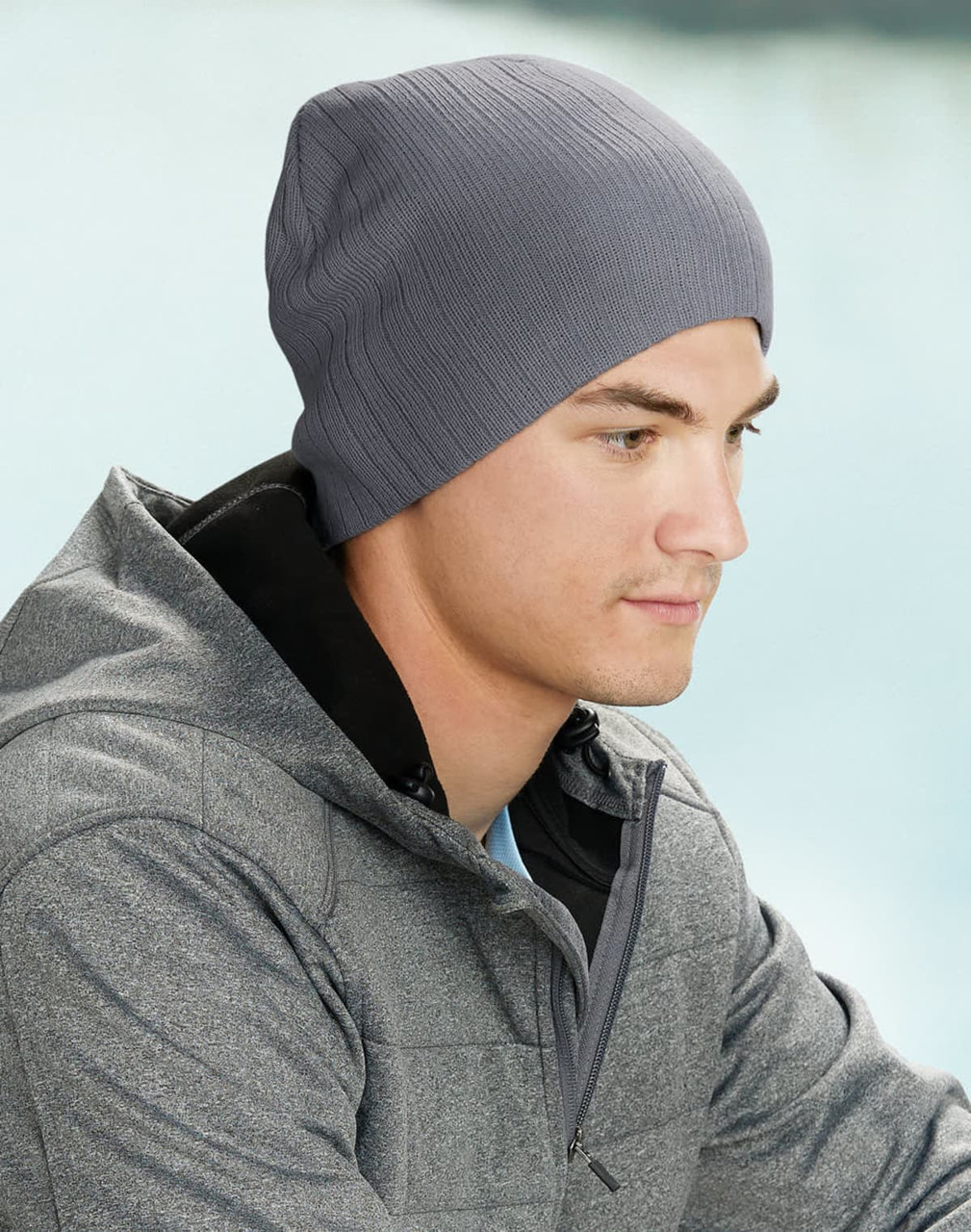 A grey cable knit beanie worn by a man in a grey jacket, set against a soft background.