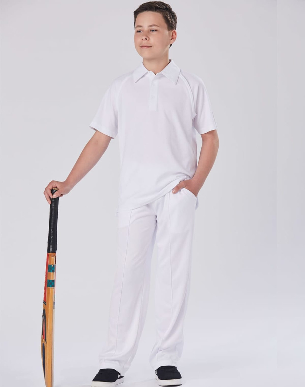 A pair of white kids' cricket pants displayed on a model holding a cricket bat, set against a plain background.