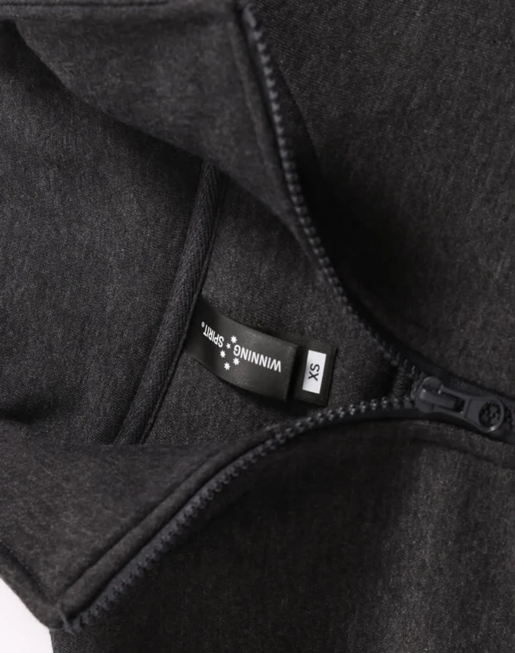 A 1/2 zip collar fleecy jumper in dark grey, featuring a hang tag and a zip closure. It has a logo.