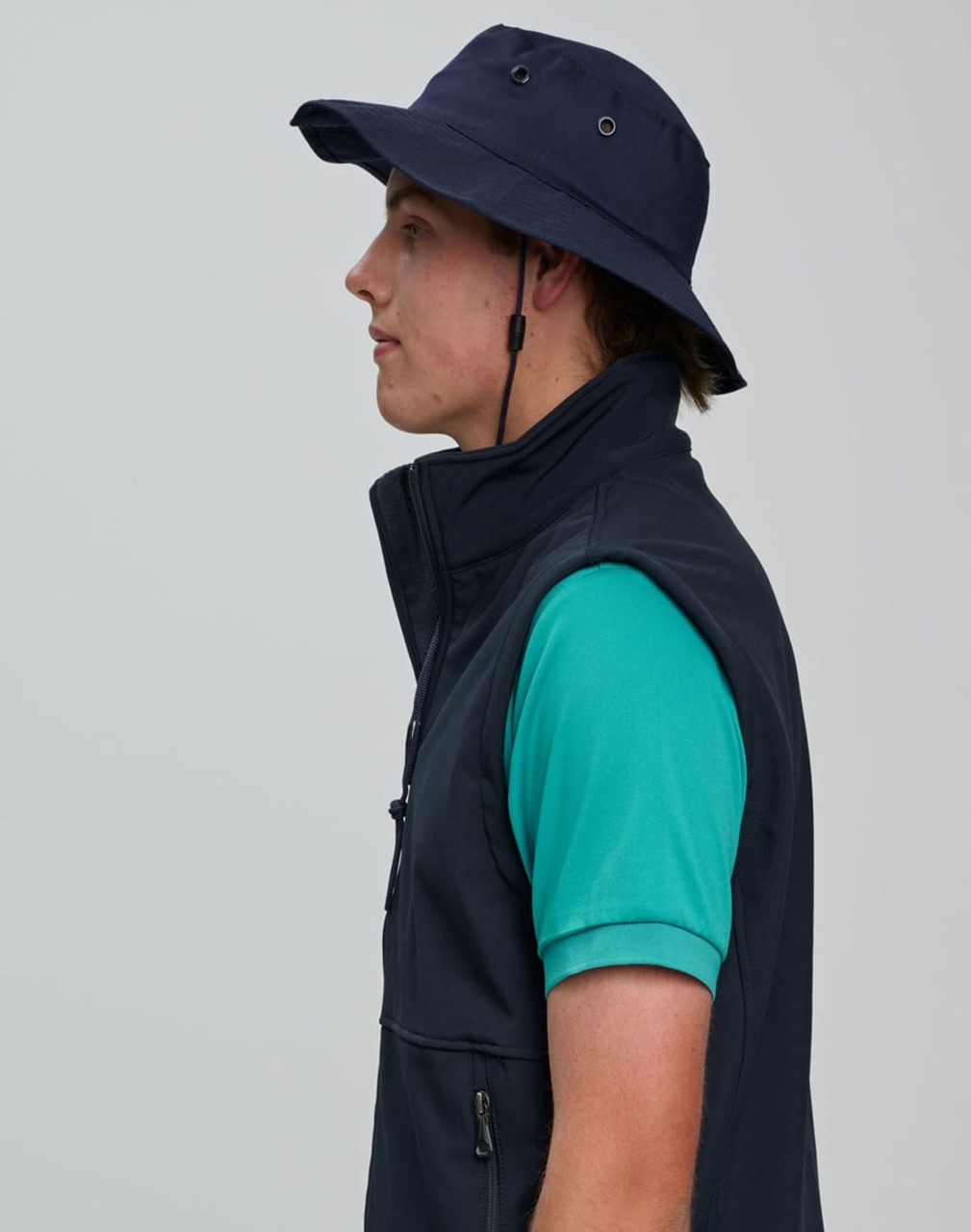 A navy blue bucket hat with a clip-on chin strap, worn by a person in a green shirt and black vest.