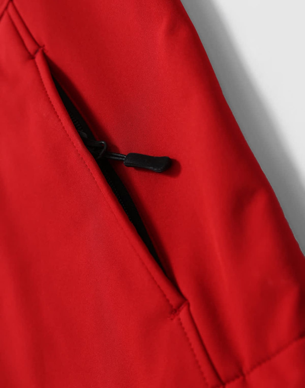 A close-up view of a red softshell fabric with a zippered pocket detail. The fabric appears smooth and durable.