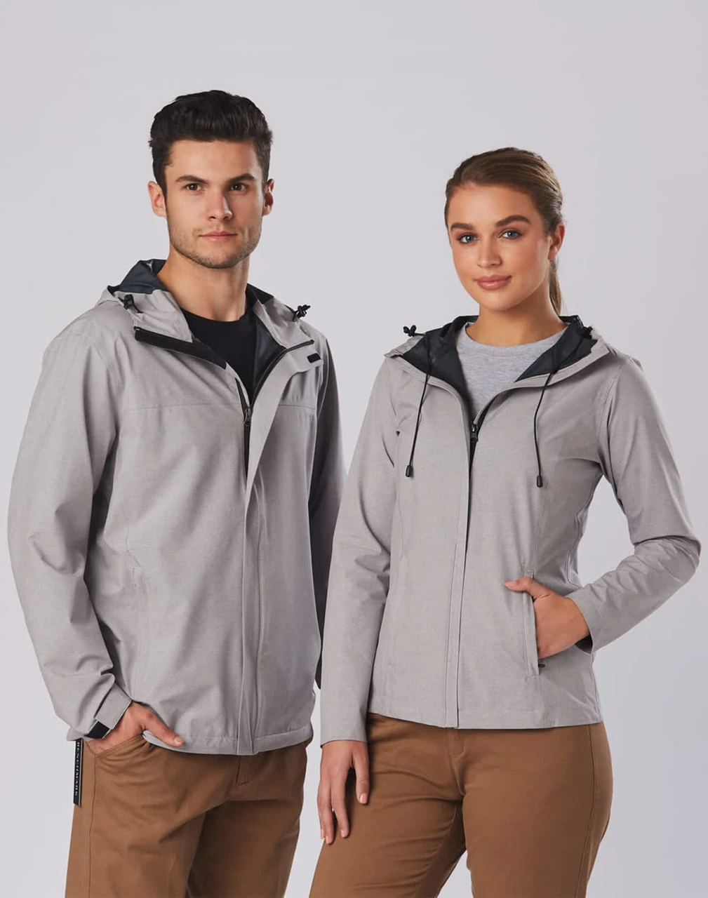 A grey men's waterproof performance jacket with a hood, featuring a logo, displayed on a male and female model.