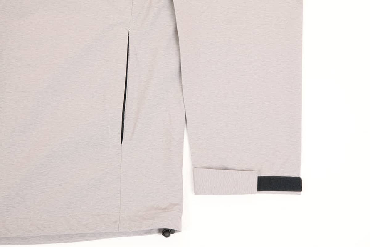 A light grey men's waterproof performance jacket featuring a zipped pocket and adjustable cuffs. The jacket includes branding.
