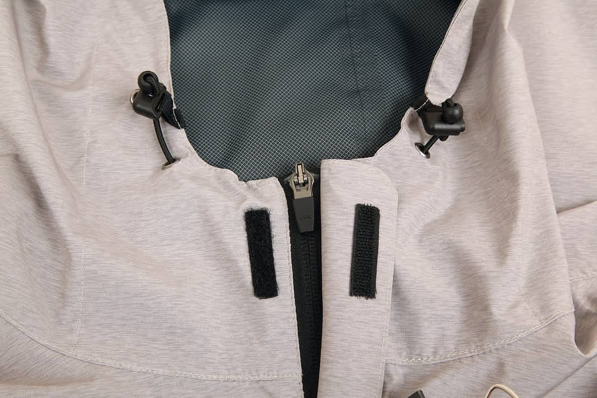 A close-up of a light grey waterproof performance jacket, featuring adjustable toggles and zip fastening.
