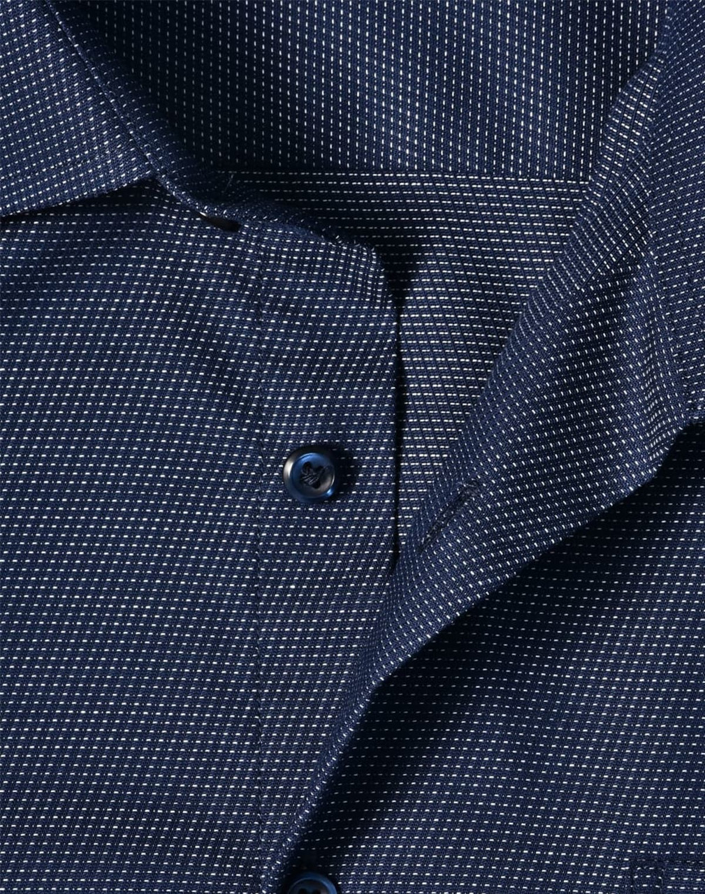 A close-up of a navy blue men's button-up shirt featuring a pin dot pattern and a collar with buttons.