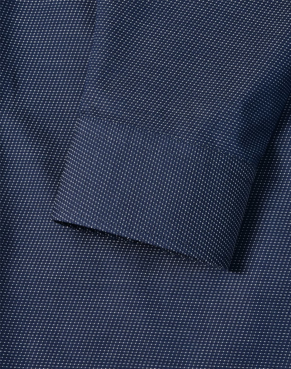A close-up of a navy men's button-up shirt featuring a pin dot pattern and a cuff detail.