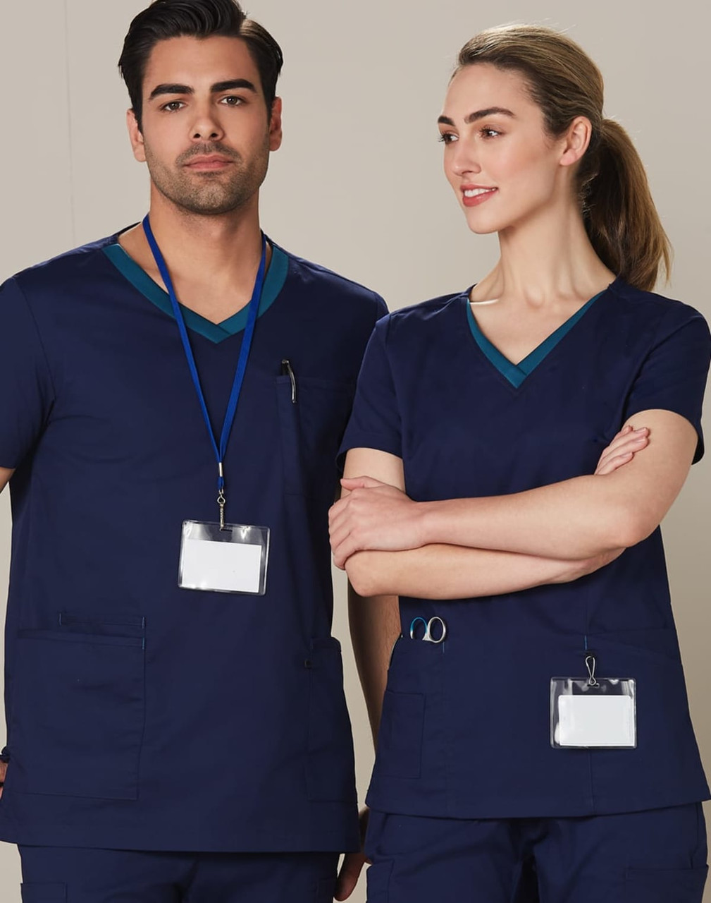 A navy scrub top with contrasting teal collar details, worn by a male and female model. Features pockets and identification badges.