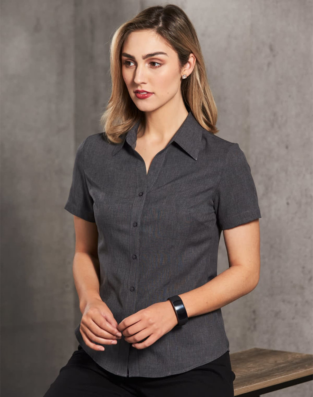 A women's short sleeve shirt in dark grey with a button-up front and collar, featuring a logo.
