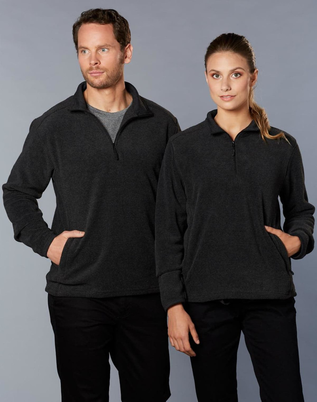 A grey half zip polar fleece pullover on two models, one male and one female, both with pockets and standing side by side.