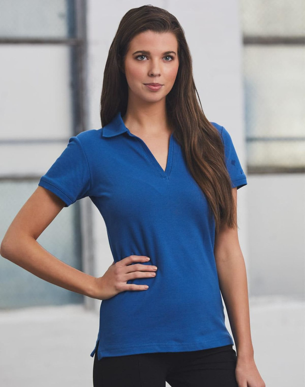 A model wearing a blue Ladies' Longbeach Polo shirt with a collar, featuring a logo.