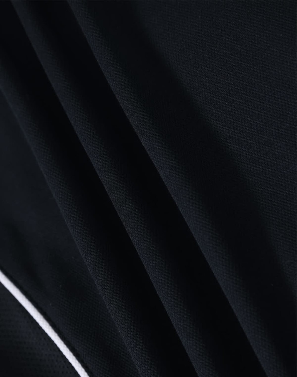 A close-up of a black polo shirt fabric, featuring a smooth texture and white detailing. The shirt has a logo.