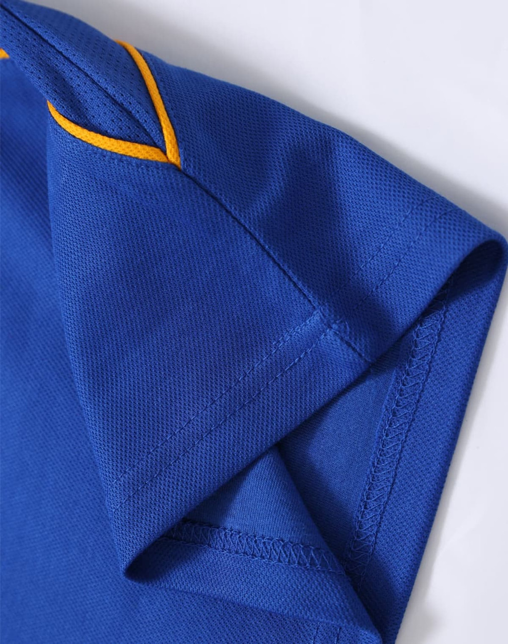 A close-up of a blue polo shirt featuring yellow stitching, showcasing the sleeve and collar detail.