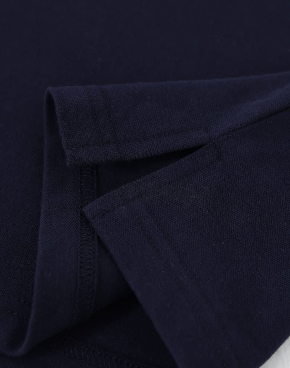 A close-up of a navy blue cotton stretch polo shirt, showcasing the fabric and folded sleeves. It features a logo.