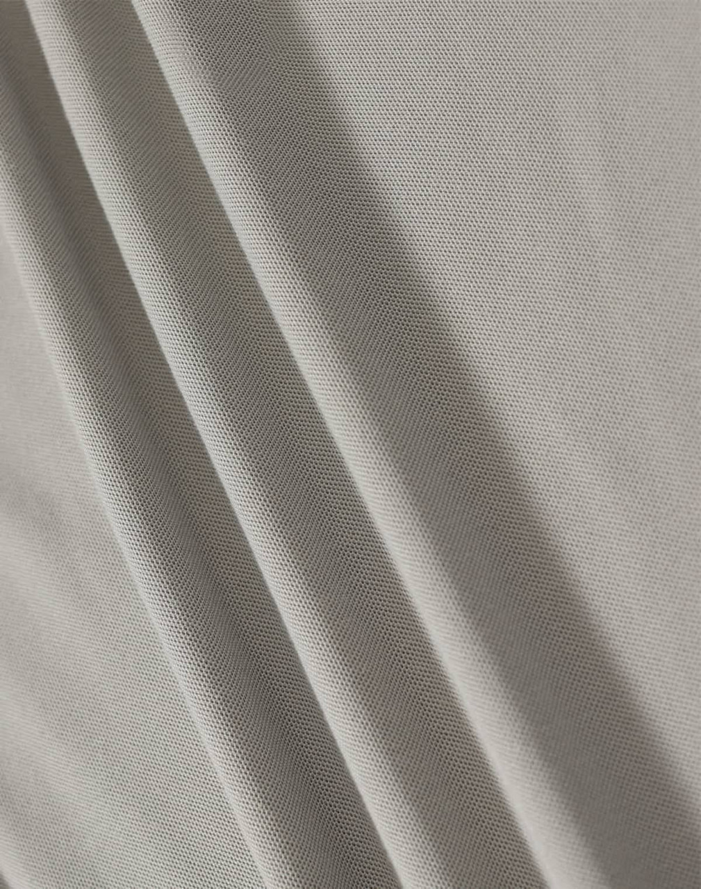 A textured, light grey fabric featuring soft folds. The material is suitable for polo shirts and has a subtle sheen.