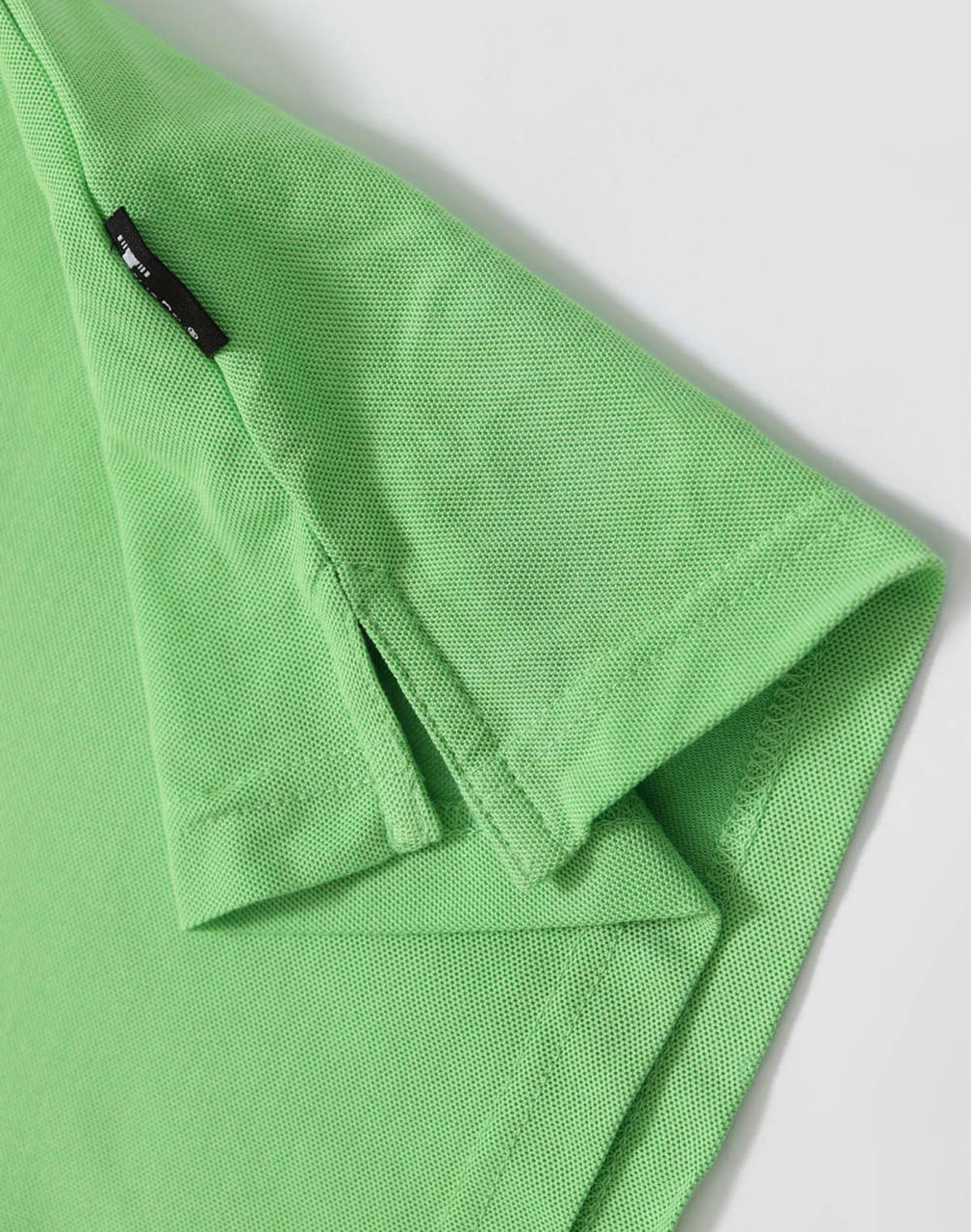 A green polo shirt featuring a logo and a textured fabric. Close-up of the collar and sleeve hem.