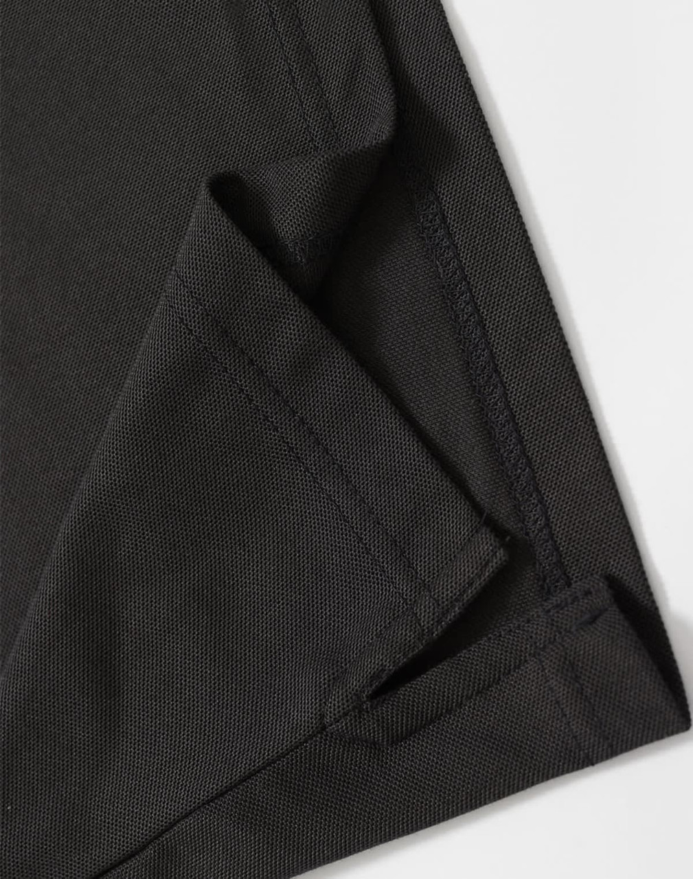 A close-up of a black polo shirt featuring a neatly stitched hem and collar. The fabric texture is visible.