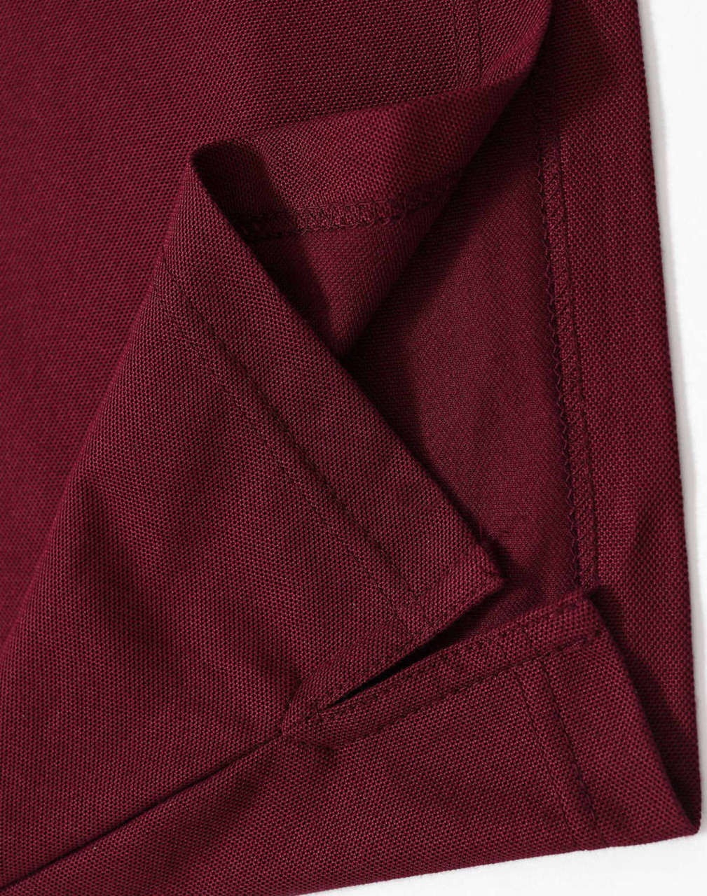 A close-up of the hem and fabric of a burgundy polo shirt, featuring a logo on one side.