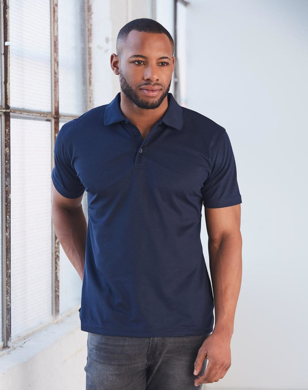 A man models a navy blue short-sleeved polo shirt, featuring a collar and a logo on the chest.