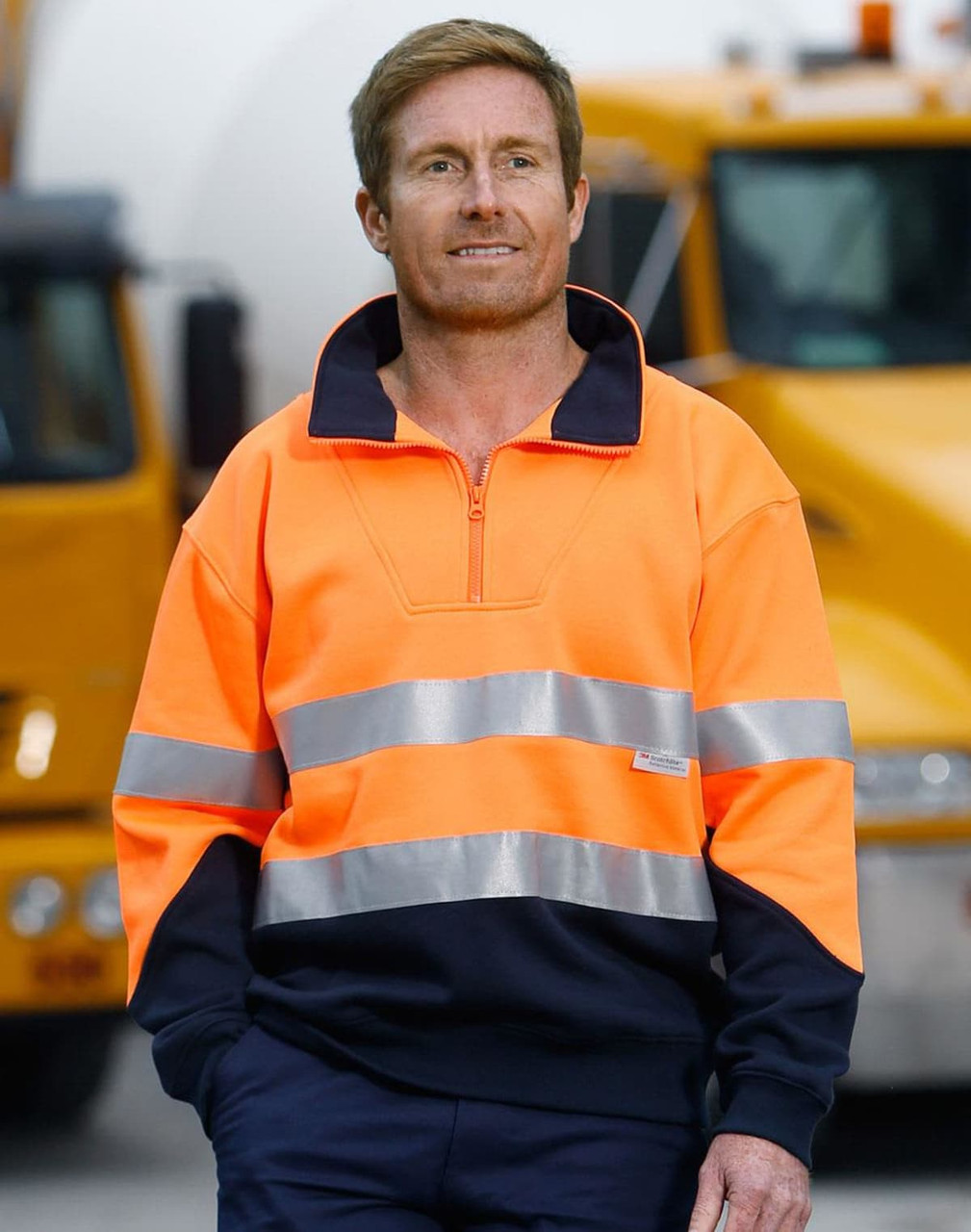 Hi-Vis long-sleeve fleece collar sweater in orange with reflective strips, paired with navy trousers. Features branding.