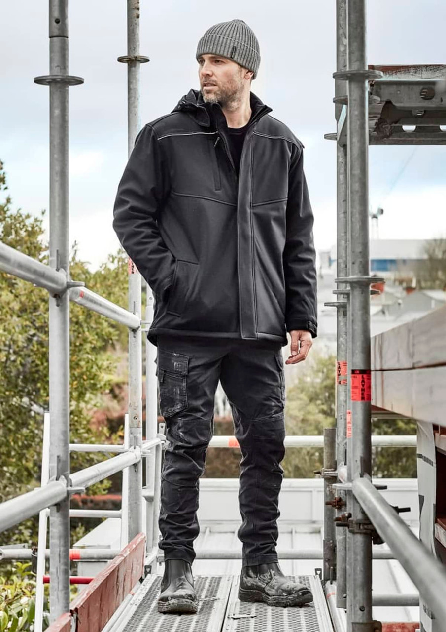 A black unisex softshell jacket worn by a man on scaffolding, with a beanie and work pants, set outdoors.