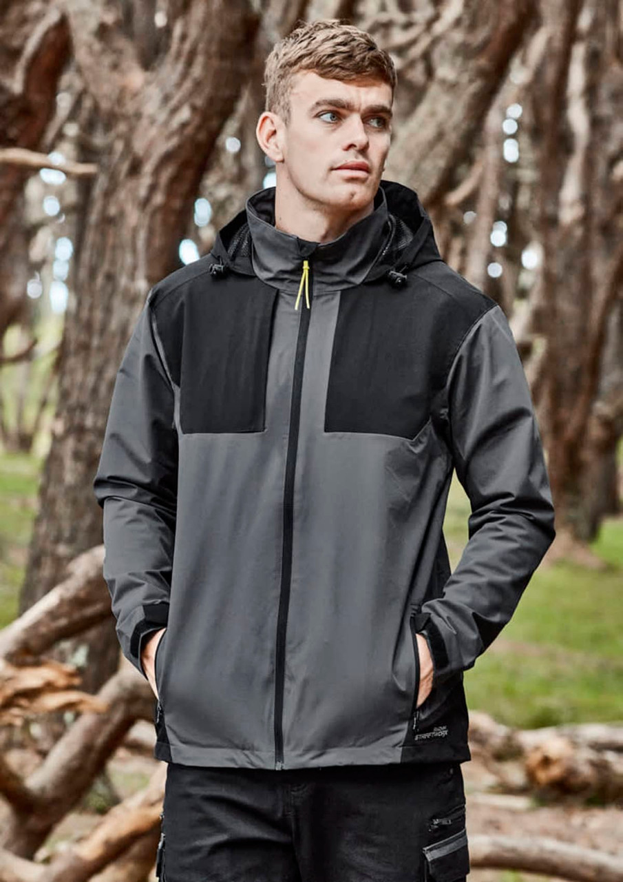 A unisex waterproof jacket in grey and black features a hood and branding. Set against a natural background with trees.