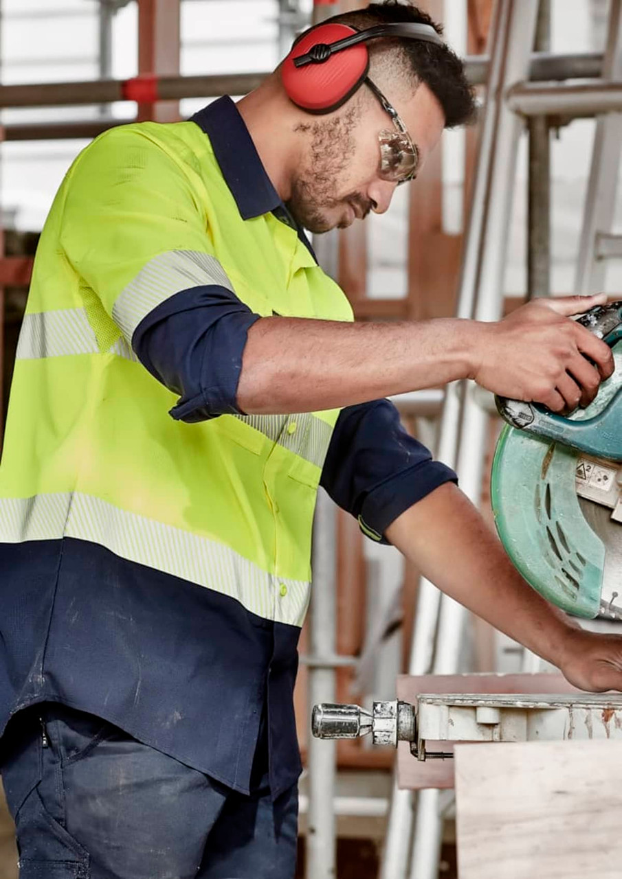 A segmented long sleeve work shirt in hi-vis yellow and navy, featuring reflective tape and a logo, worn by a male worker.