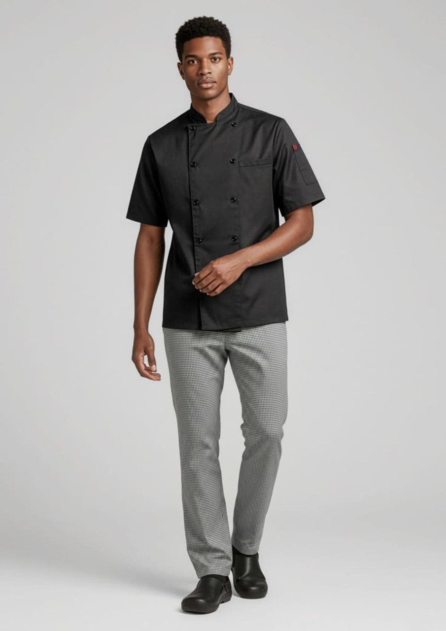 A model wearing a black short-sleeve chef jacket and grey pants, walking in a neutral background. The outfit features a logo.
