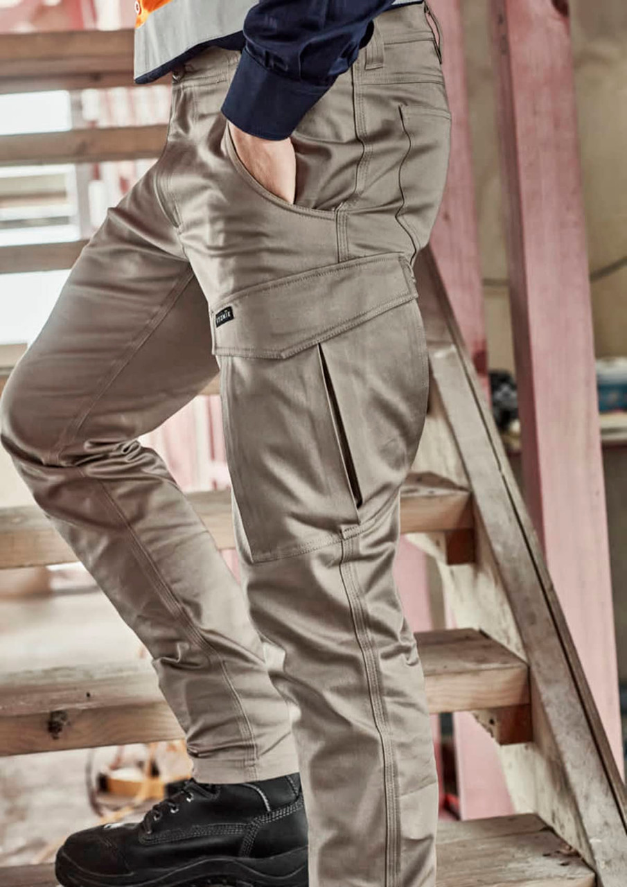 A model wearing beige cargo pants, featuring multiple pockets, standing on a wooden staircase.