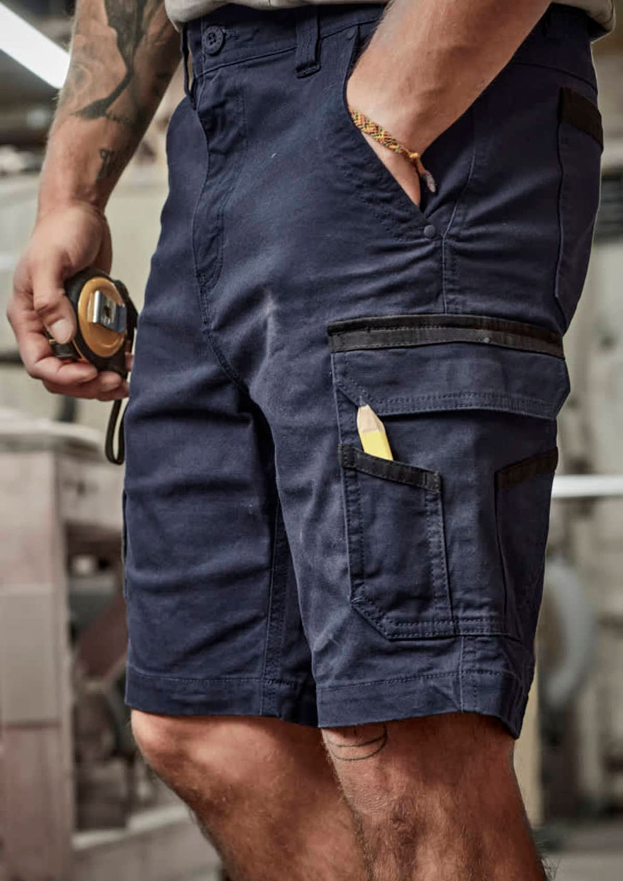 Navy work shorts featuring multiple pockets and a small tool. Close-up of model holding a measuring tape.