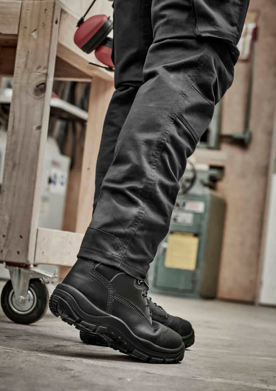 A pair of black rugged cooling stretch pants paired with black boots, set in an industrial environment.