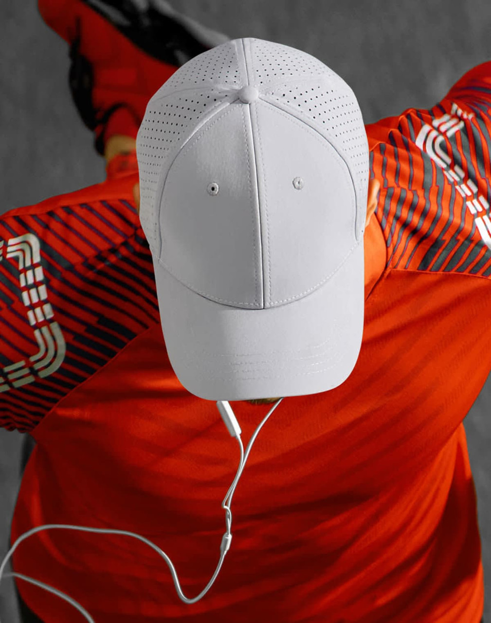 A white cap with laser cut detailing, positioned on a red shirt, featuring a logo.
