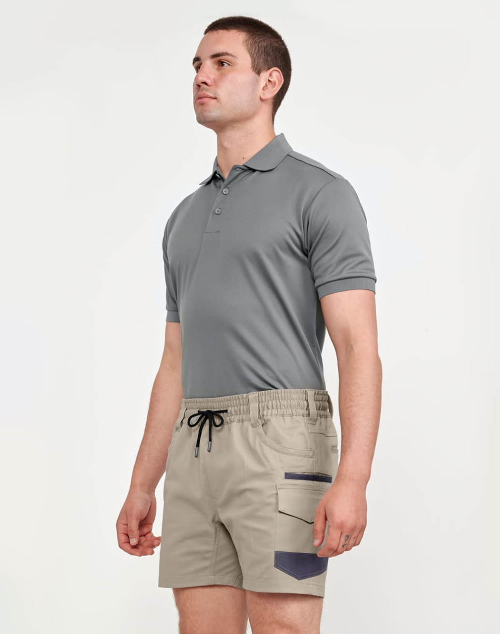 A man wearing a grey polo shirt and beige stretch drill work shorts with a logo. The shorts feature side pockets.