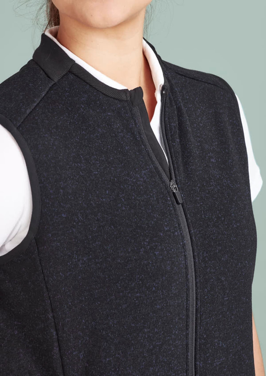 A black zip front vest featuring a high collar and a fitted design, with a white shirt underneath.