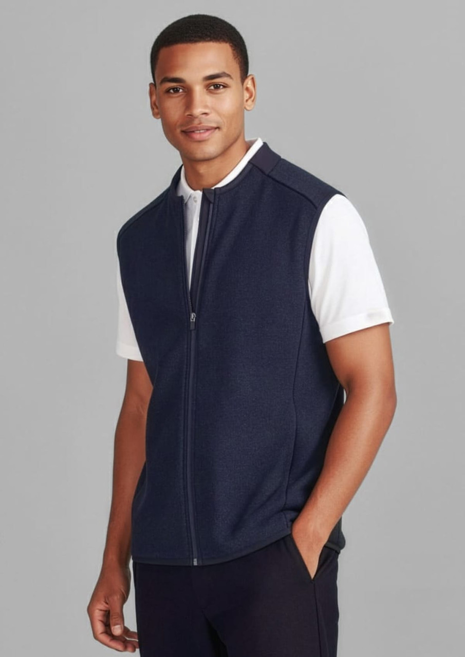 A navy zip-front vest is worn over a white shirt. The model stands against a grey background, featuring a logo on the vest.