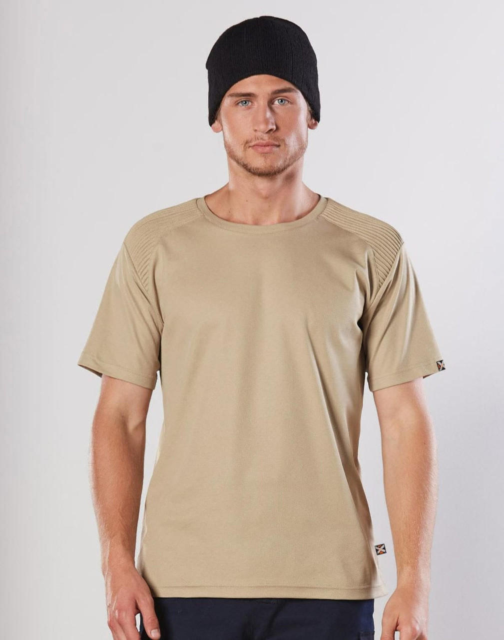 A beige short-sleeve work t-shirt with a textured shoulder design, worn by a model in a black beanie.