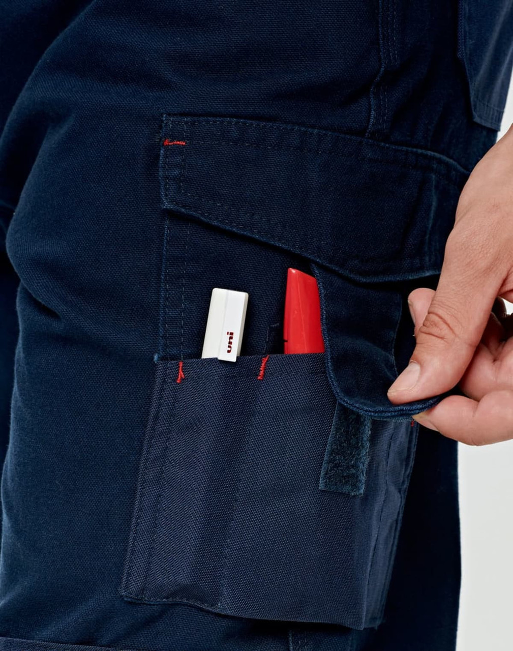 A pair of navy work pants with pockets, featuring red stitching and a hand reaching into a side pocket.