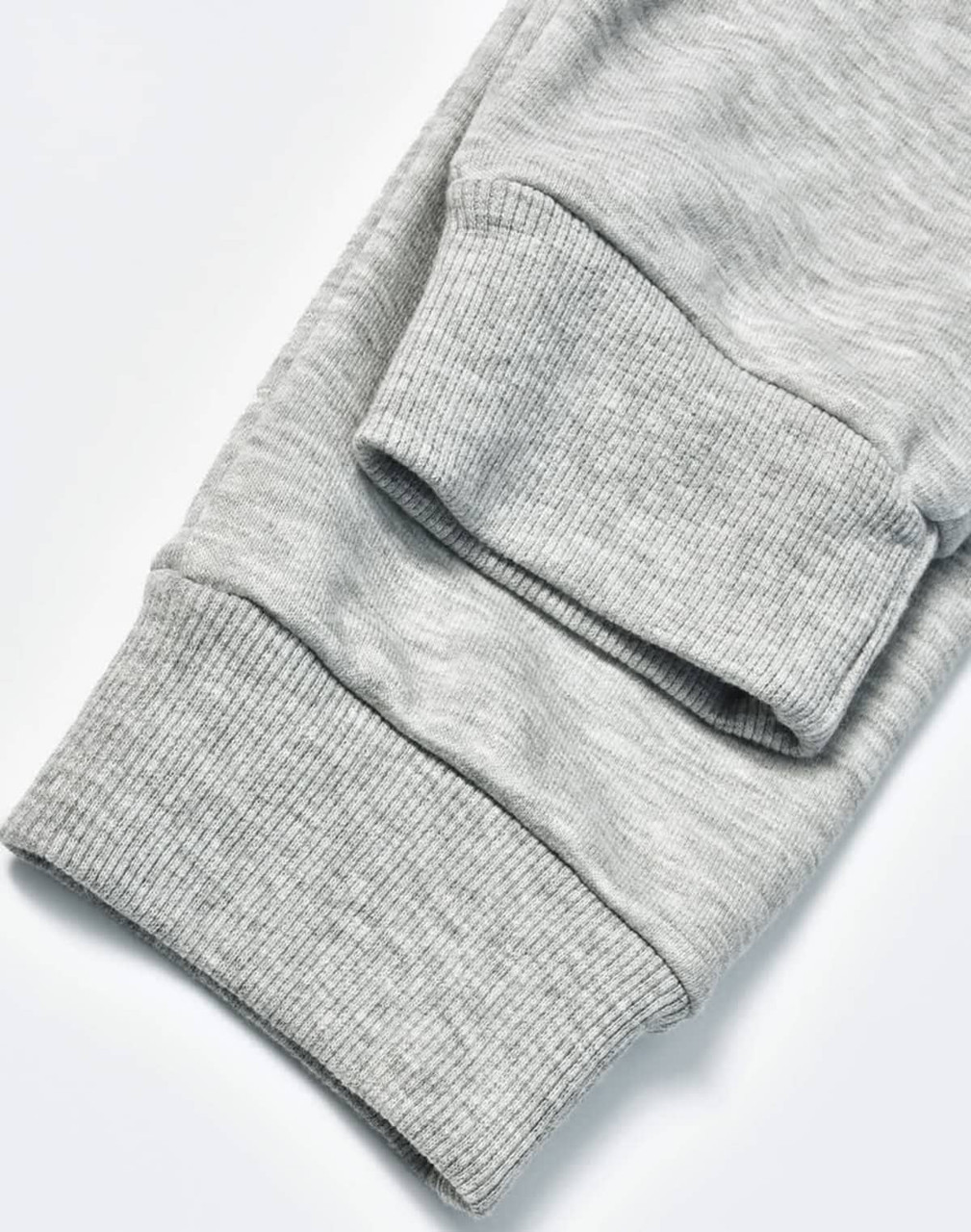 A pair of grey poly/cotton terry sweat pants with ribbed cuffs. The image highlights the fabric texture.