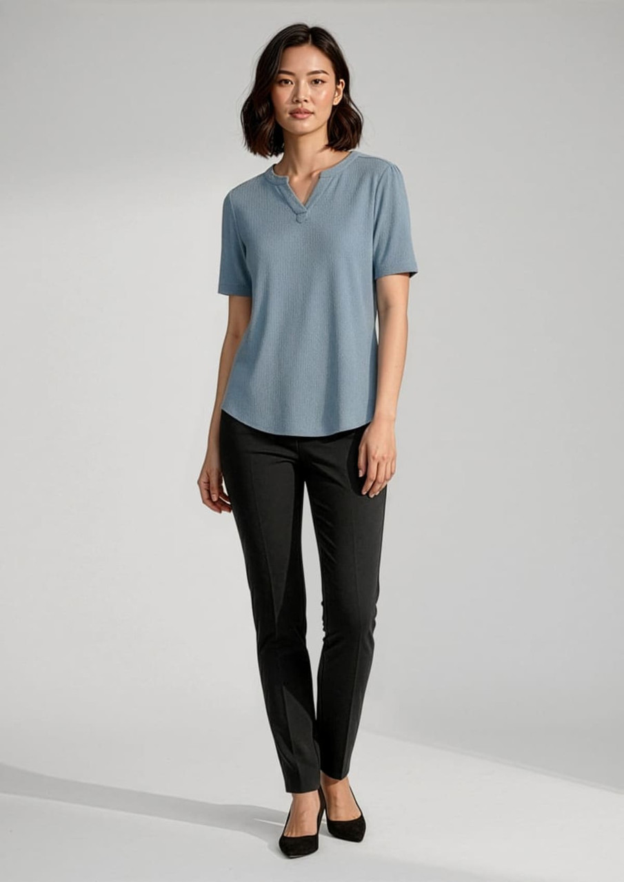 A blue short sleeve blouse on a model, paired with black trousers and black shoes. The blouse has a subtle neckline detail.