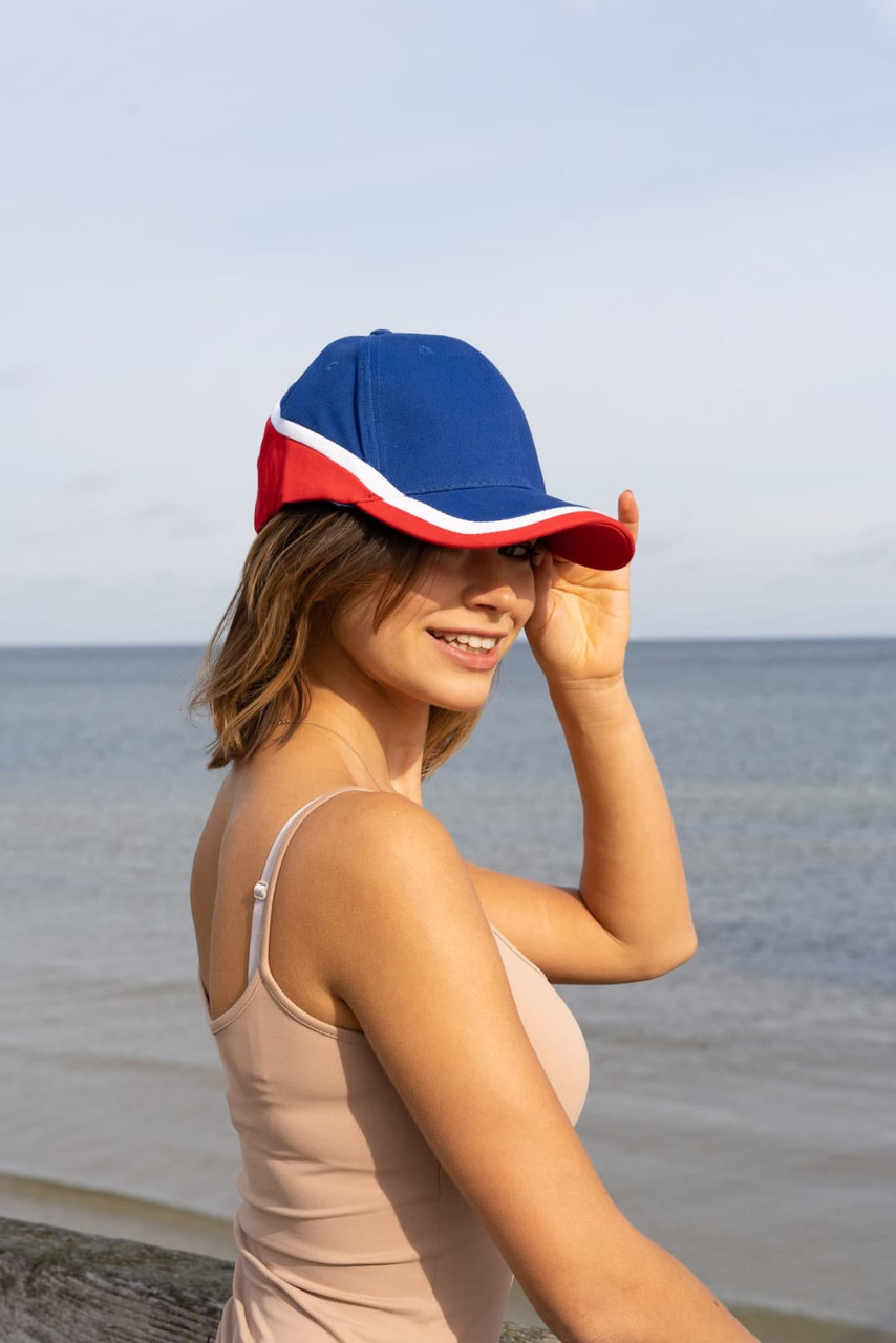 A tri-coloured cap in blue, red, and white, featuring a logo, worn by a woman at the beach.