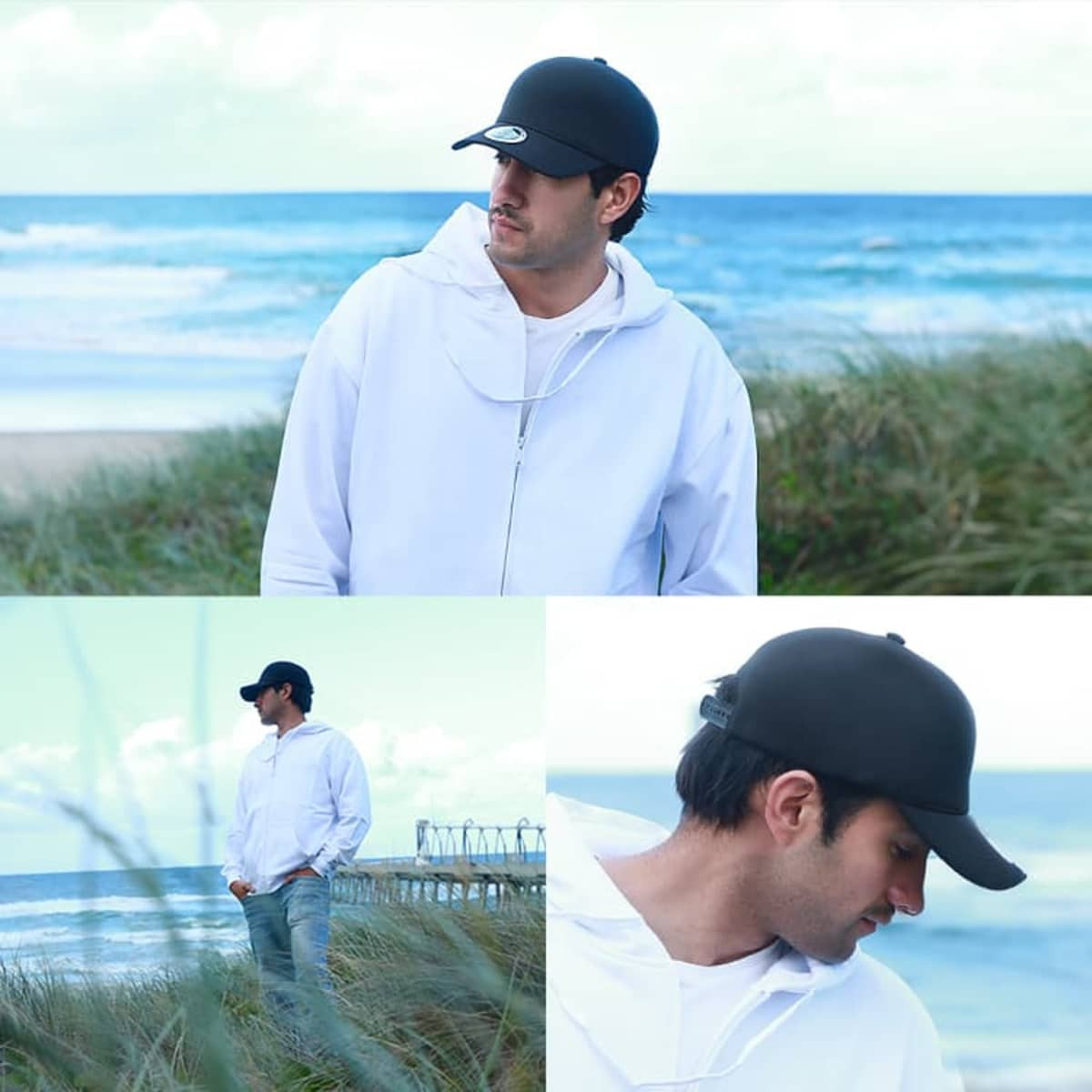A black cap worn by a man in a white hoodie, standing by the beach with waves in the background.