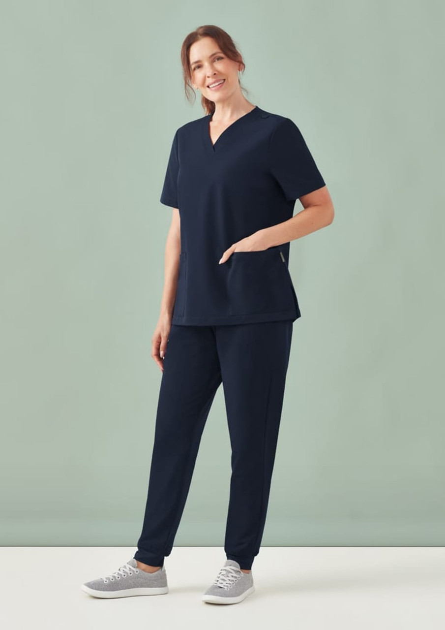 A navy women's V-neck scrub top and matching pants displayed on a model against a light green background.