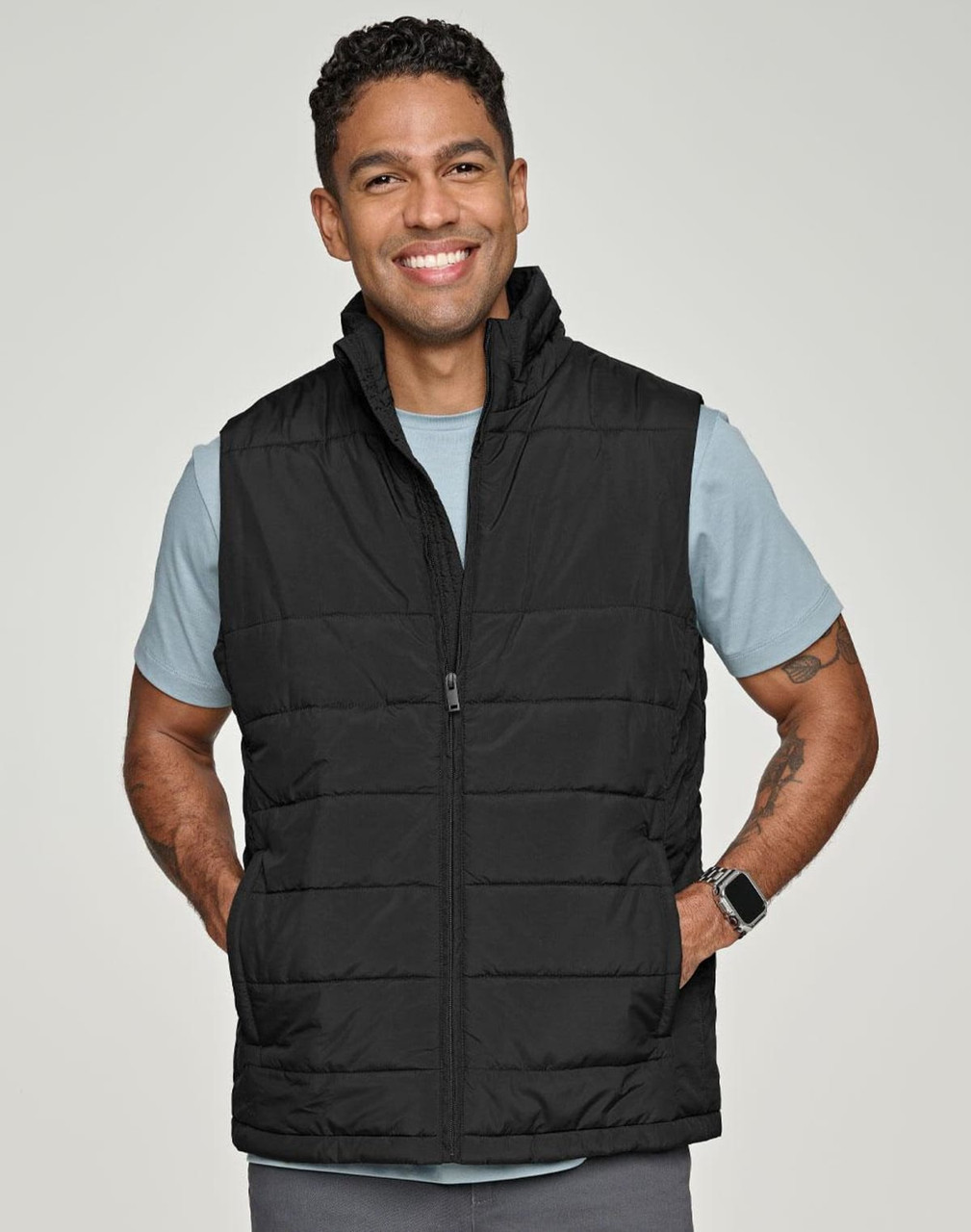 A man wearing a black insulated puffer vest with a 3D cut over a grey shirt, smiling. The vest has a logo.