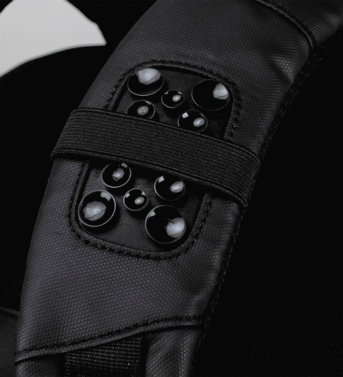 A close-up of a black backpack strap featuring a textured panel with multiple glossy round embellishments.