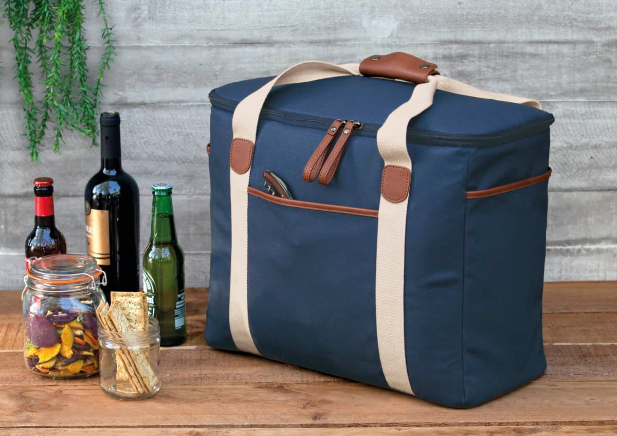 A navy cooler bag with beige straps sits next to several bottles of wine and beer, and a jar of snacks.