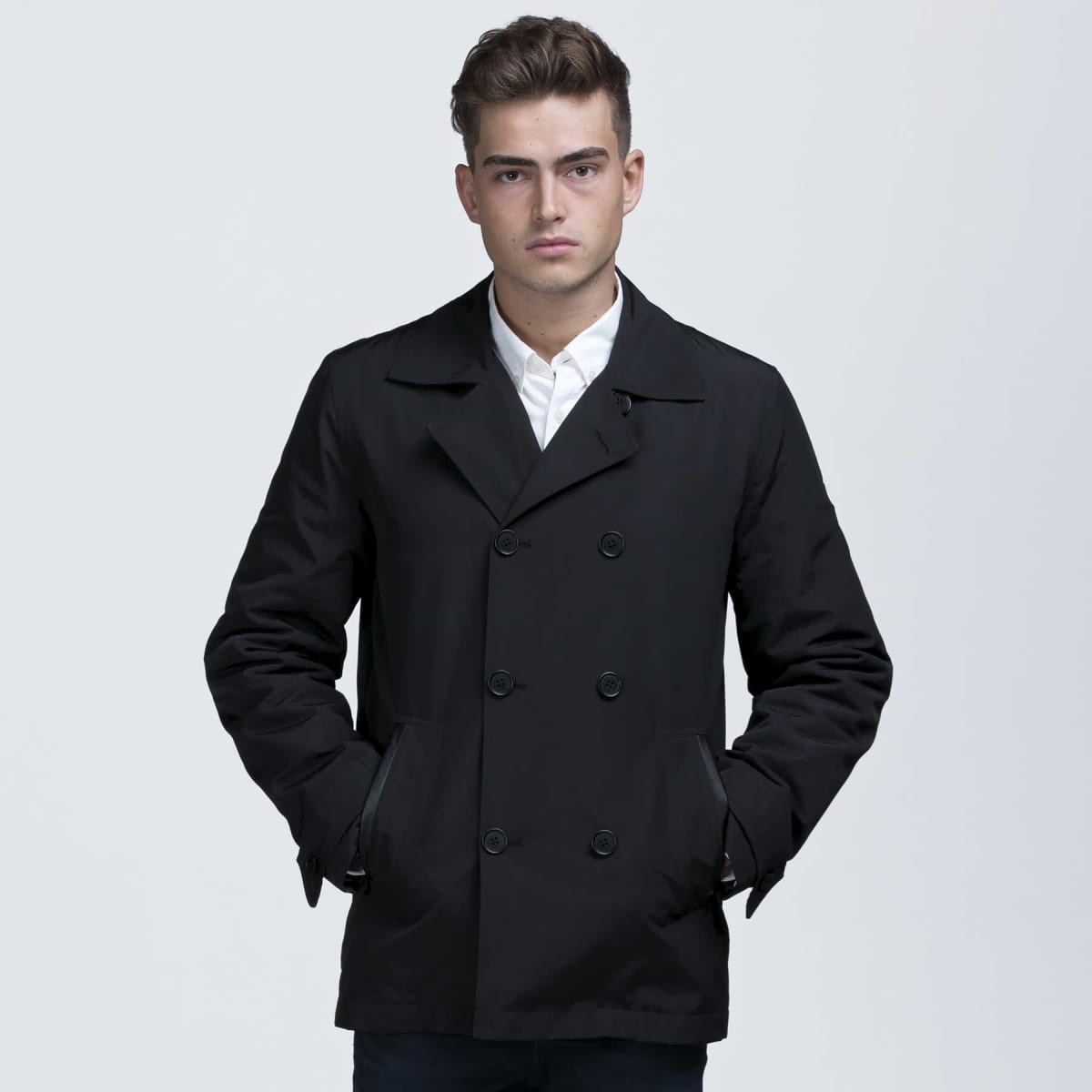 A black trench coat featuring a double-breasted design and side pockets, worn by a model.