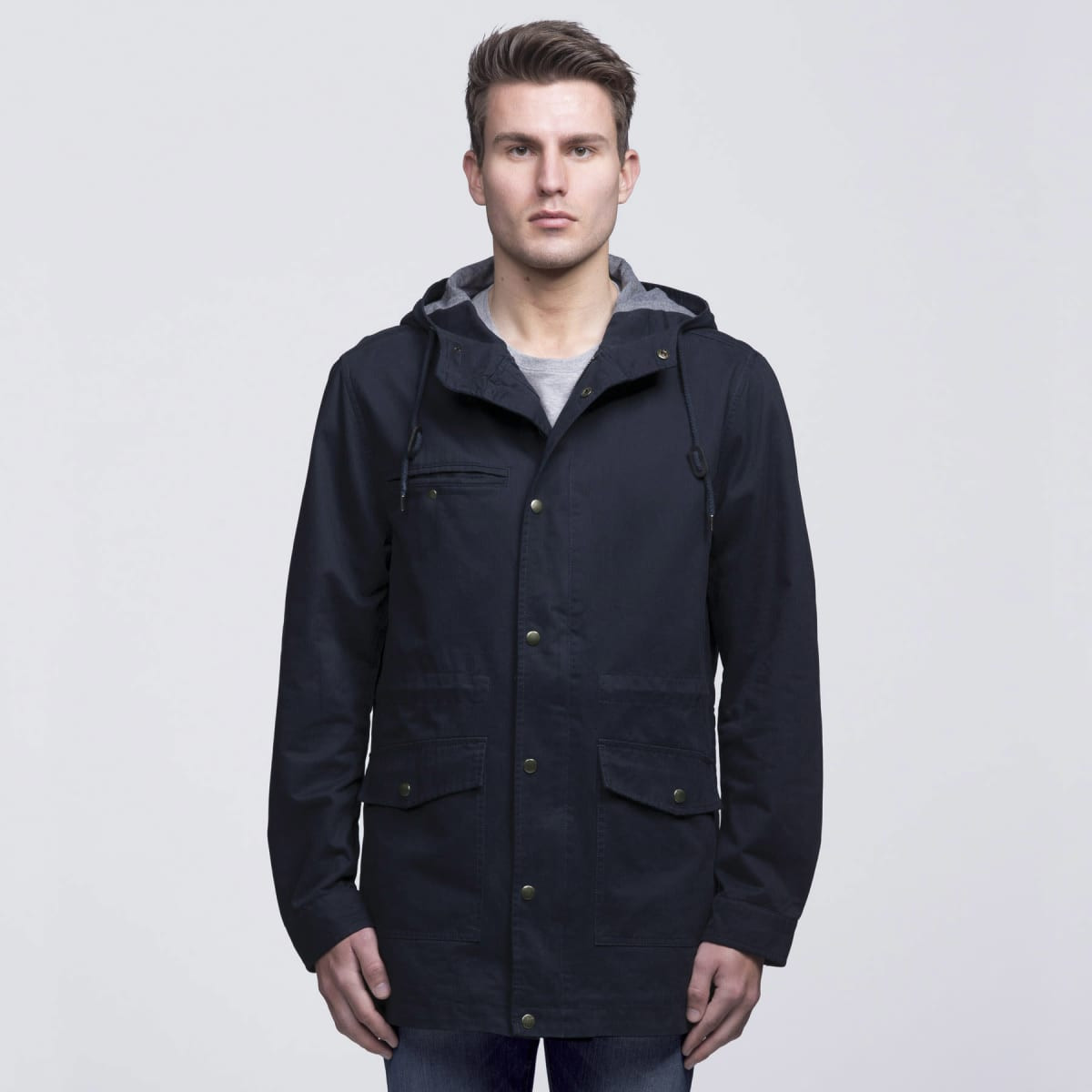 A navy blue twill jacket with a hood, featuring pockets and a grey lining, worn by a model.
