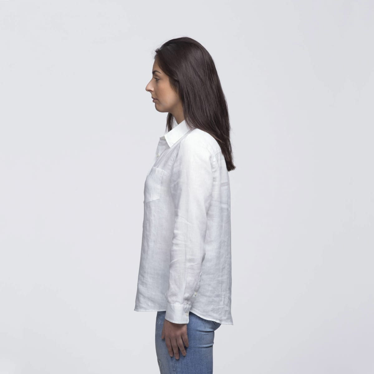 A white linen button-up shirt displayed on a model from the side, featuring a pocket and a collar.